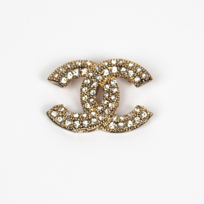 Brosje i gullfarget metall - dobbel C-form med strass 4 x 3 cm